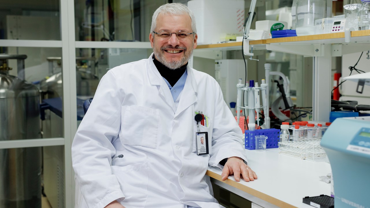 Gruppledare Peter Andersen sitter vid en labbänk i sitt labb och ler glatt.
