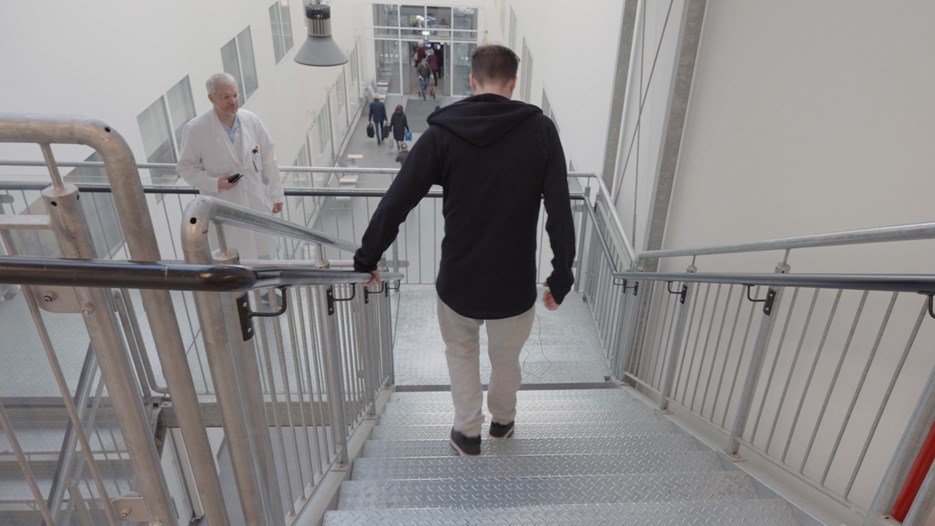 Överläkaren i neurologi och professorn Peter Andersen observerar sin ALS-patient som går ned för en av trapporna på Norrlands universitetssjukhus.