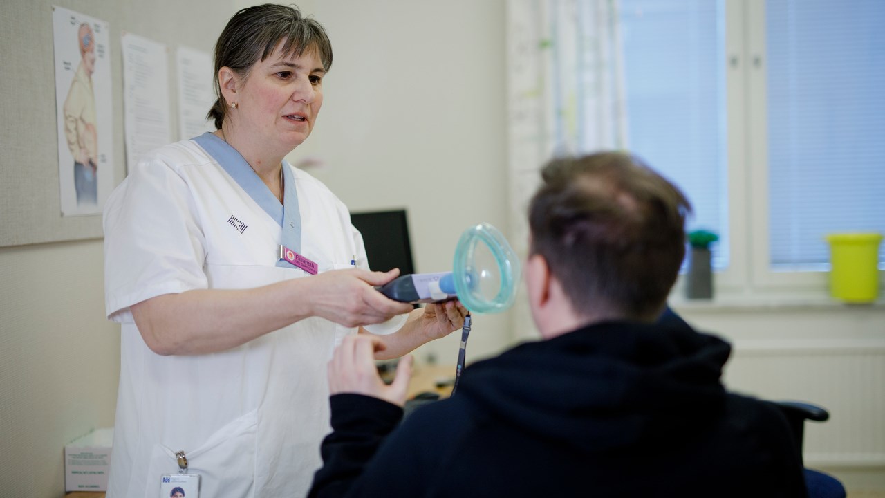 Forskningssjuksköterskan Elisabeth Müller Granberg håller fram en spirometer som ska testa ALS-patientens lungfunktionskapacitet.