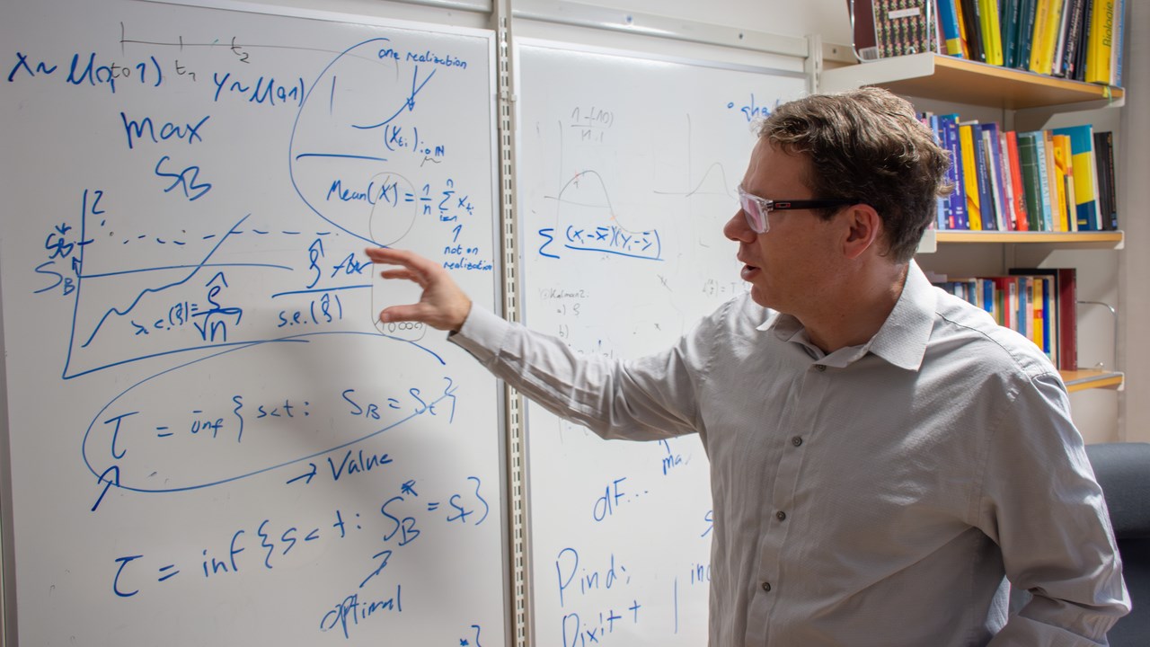 Christian Ewald pekar på matematiska formler på whiteboarden i sitt arbetsrum.