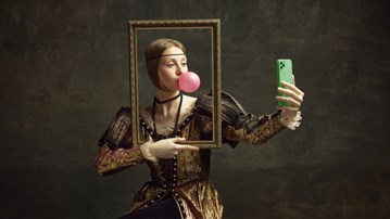 Bild på en kvinna klädd i medeltida kläder. Hon håller i en tavelram samtidigt som hon tar en selfie.