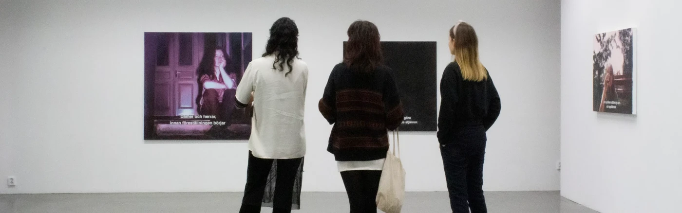 Tre personer i ett galleri som tittar på målningar