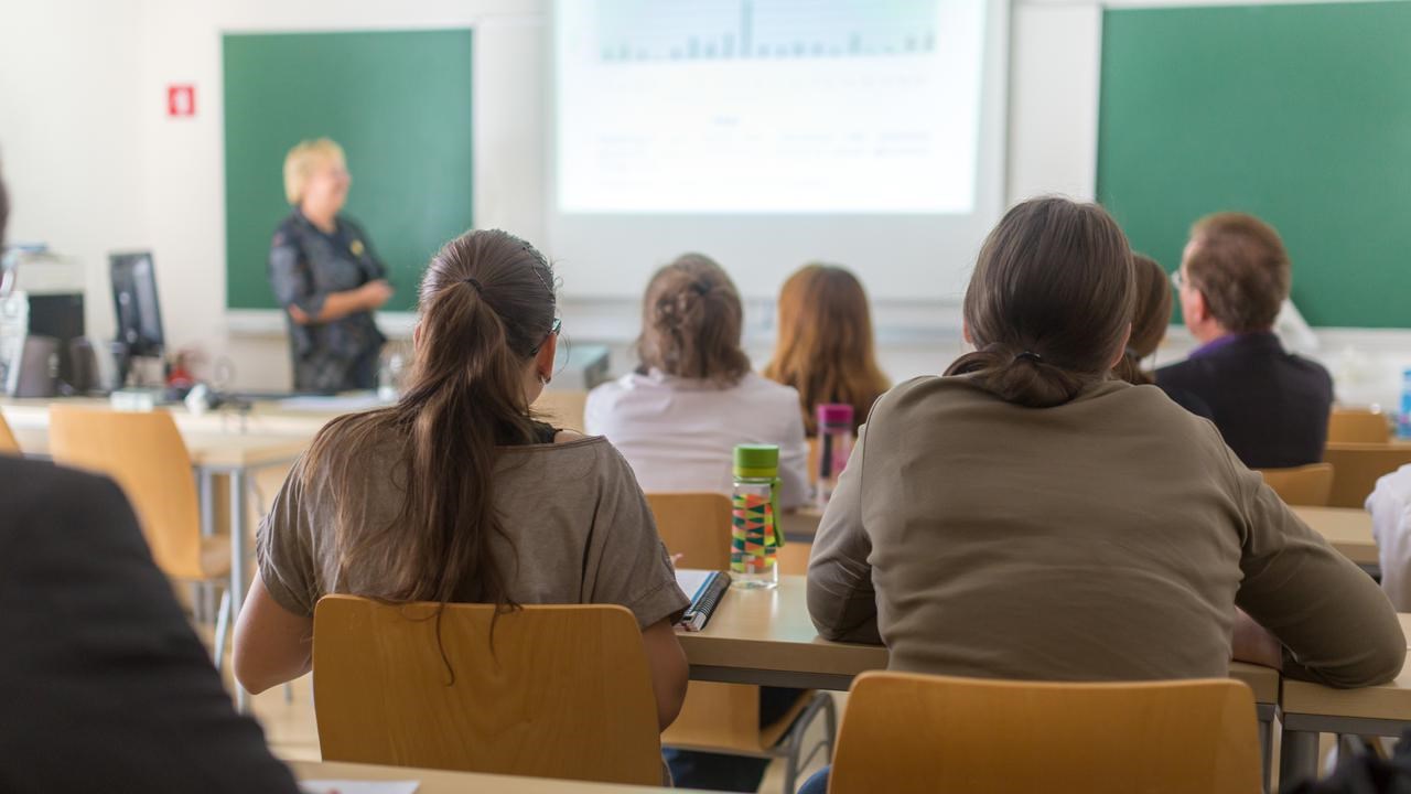 Föreläsningssal på universitet med studenter i förgrunden och en lärare vid tavlan.