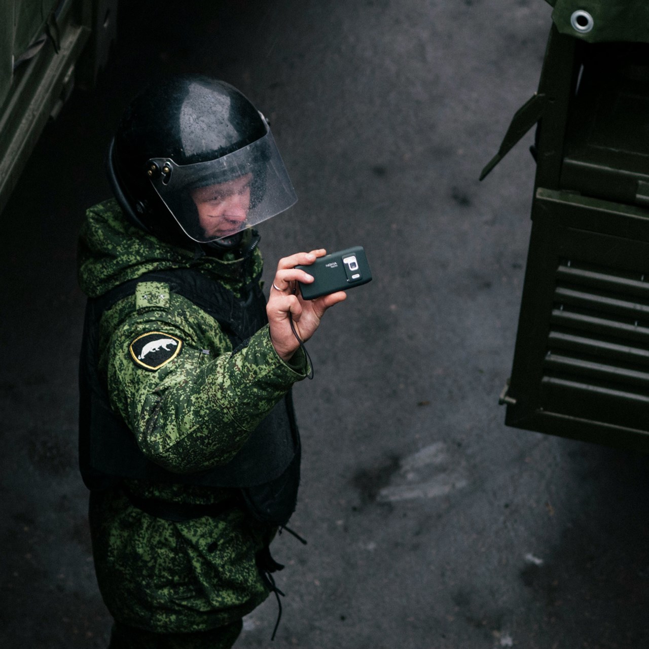 En man i grön uniform som håller en mobiltelefon.