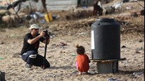 En man som fotograferar en liten flicka på stranden.