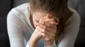 Kvinna som inte mår bra sitter lutad framåt med händerna knäppta framför ansiktet.