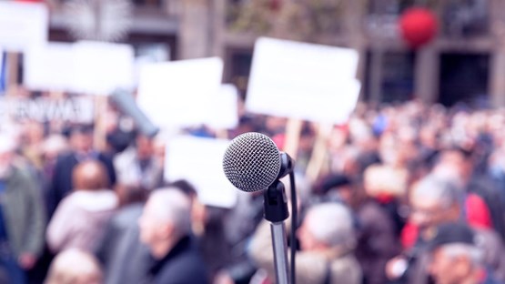 Closeup of a microphone with a crowd of protestors blurred in the background.