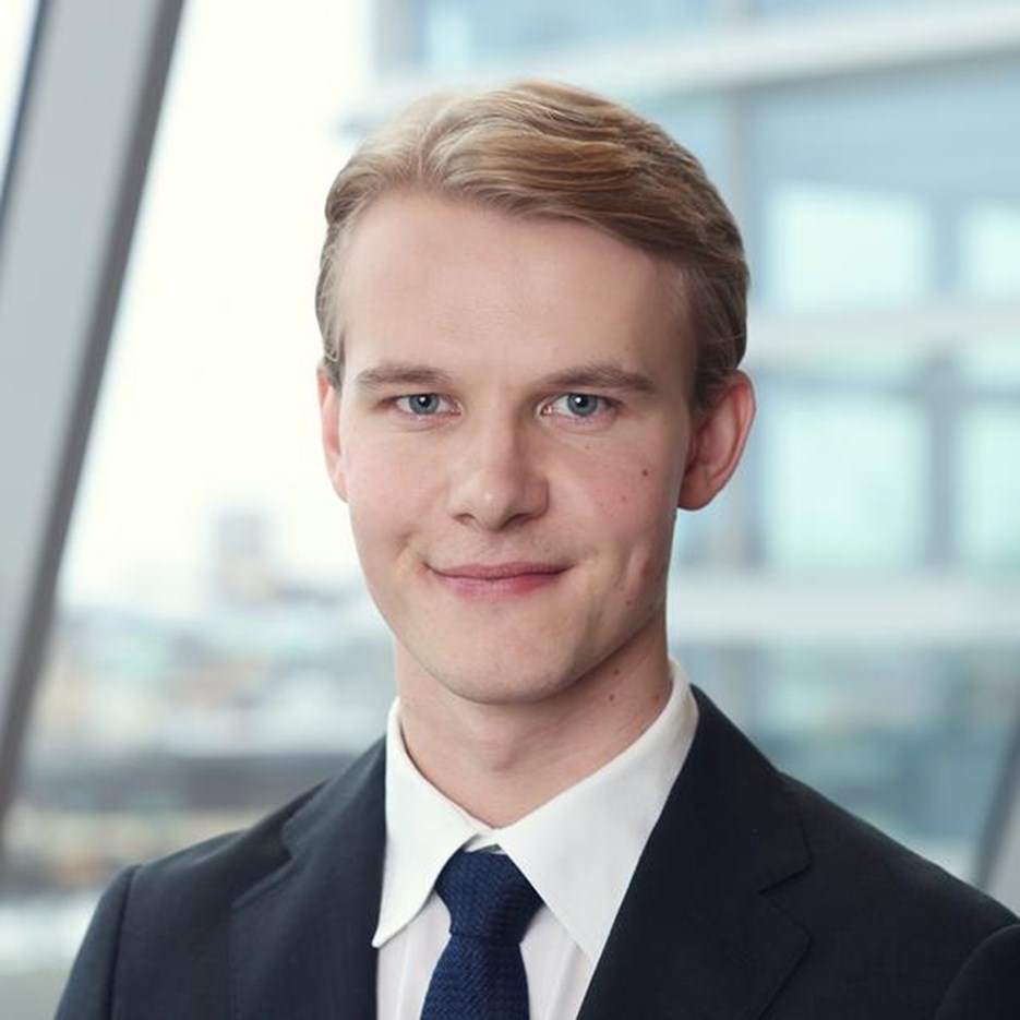 Simon Hallin, i kostym och slips, står framför ett fönster.