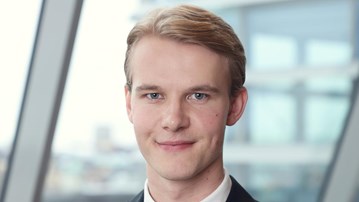 Simon Hallin, i kostym och slips, står framför ett fönster.