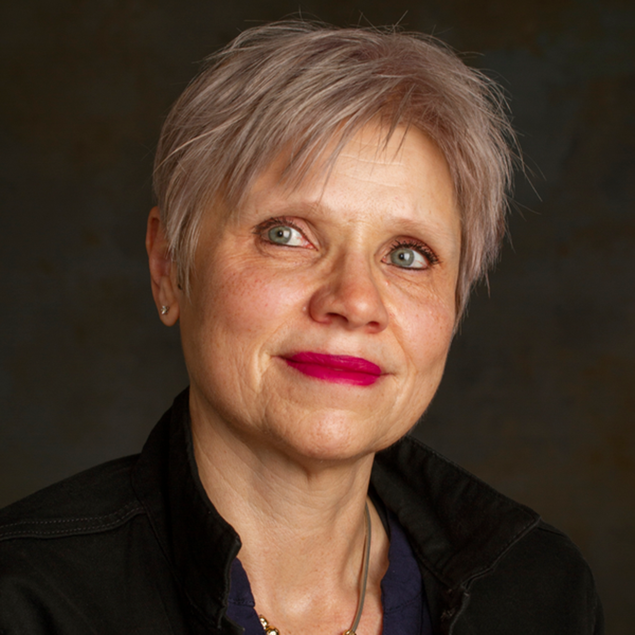 En kvinna med gr&aring;tt h&aring;r och ett halsband.