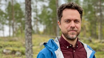 Två män som står bredvid varandra i en skog.