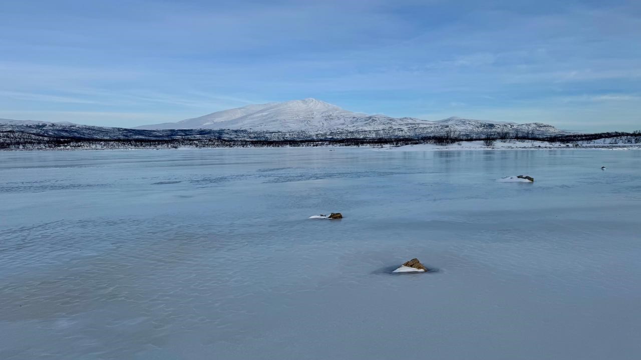 Ett fruset vattendrag med ett fjäll i bakgrunden.