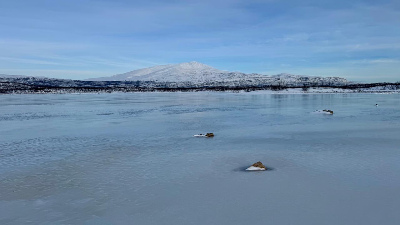Ett fruset vattendrag med ett fjäll i bakgrunden.
