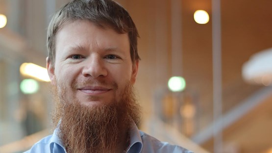 Alexandre Bartel i kort hår och skägg, står vid fönstret i ljusblå skjorta