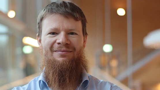 Alexandre Bartel i kort hår och skägg, står vid fönstret i ljusblå skjorta
