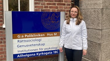 Doktorand Ekaterina Zmyvalova står bredvid en skylt utanför Lunds universitet