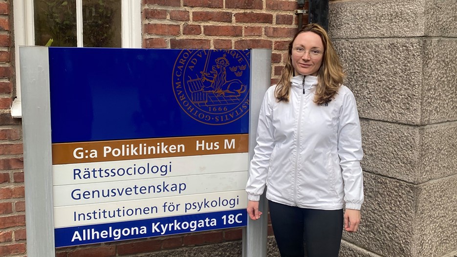 Doktorand Ekaterina Zmyvalova står bredvid en skylt utanför Lunds universitet.