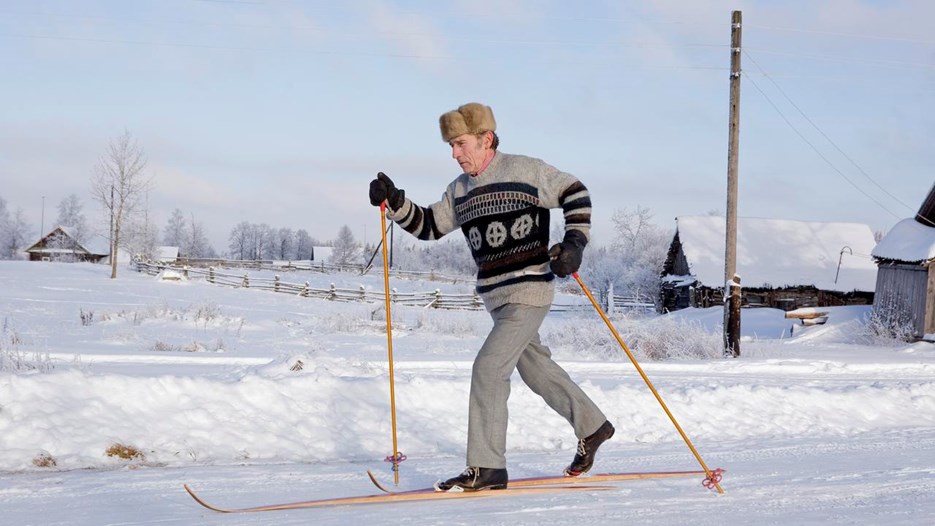 Äldre man med pälsmössa åker gammaldags skidor på landsbygd