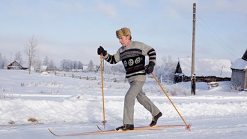 Äldre man med pälsmössa åker gammaldags skidor på landsbygd