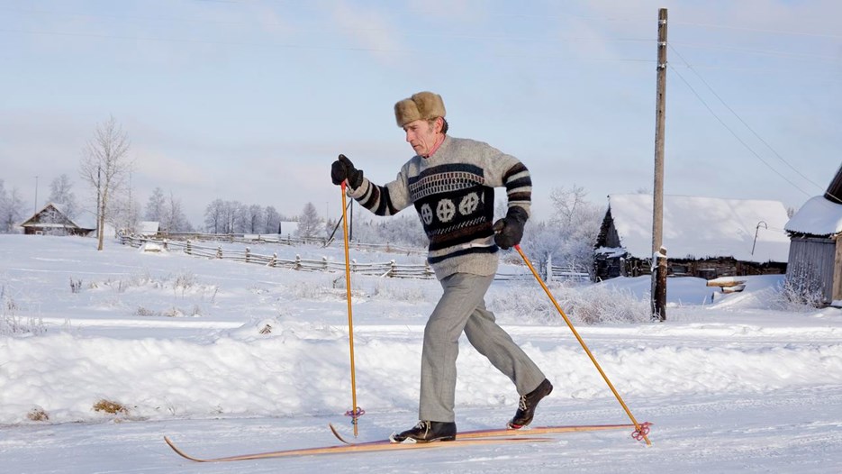 Äldre man med pälsmössa åker gammaldags skidor på landsbygd