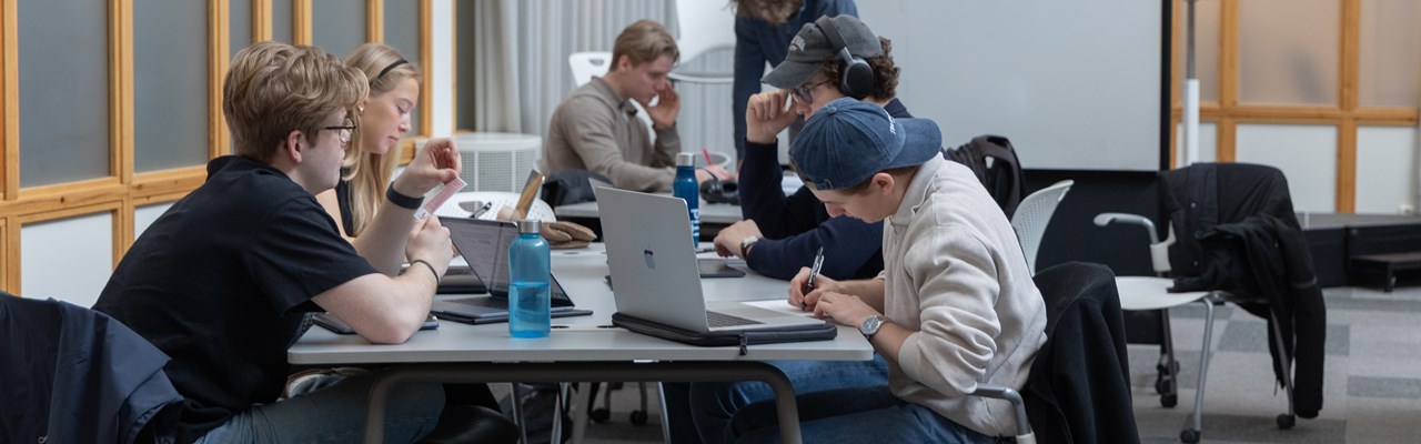En grupp studenter sitter vid ett bord med bärbara datorer.