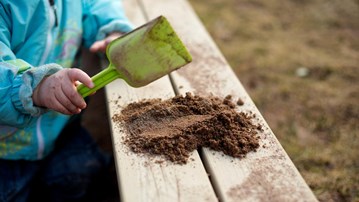 Detalj på barn på förskola som lägger upp sand med spade på kanten till sandlåda.
