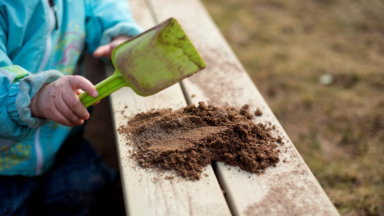 Detalj på barn på förskola som lägger upp sand med spade på kanten till sandlåda.
