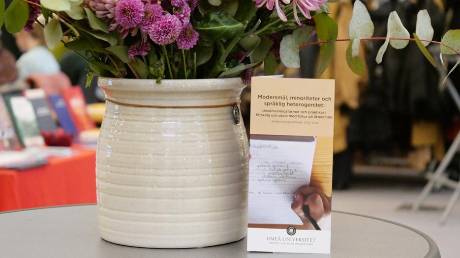 Ett ståbord med en blomkruka och en folder.