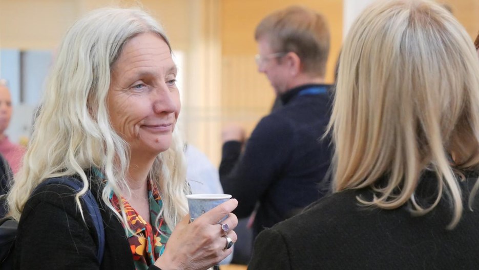 Två kvinnor pratar med varandra. En av dem håller i en pappersmugg.