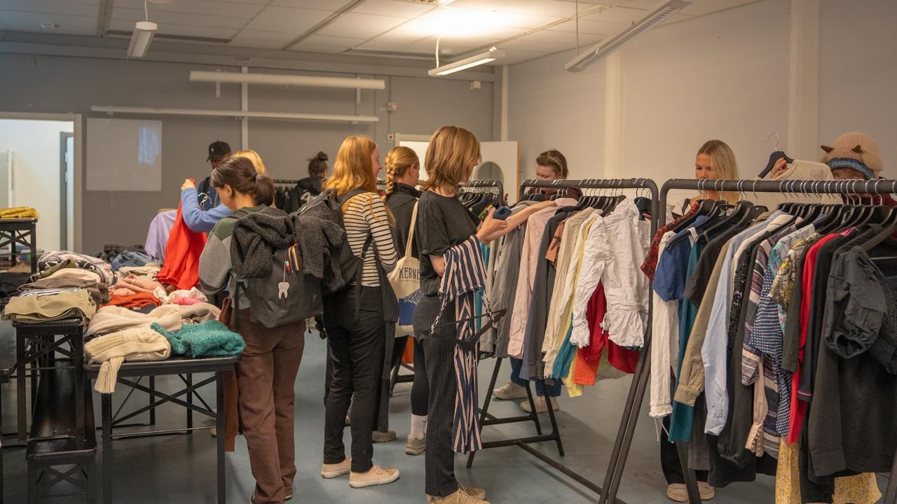 En grupp m&auml;nniskor som st&aring;r runt ett kl&auml;dst&auml;ll och tittar efter kl&auml;der.