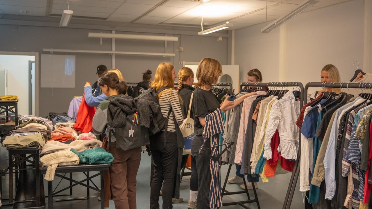 En grupp m&auml;nniskor som st&aring;r runt ett kl&auml;dst&auml;ll och tittar efter kl&auml;der.