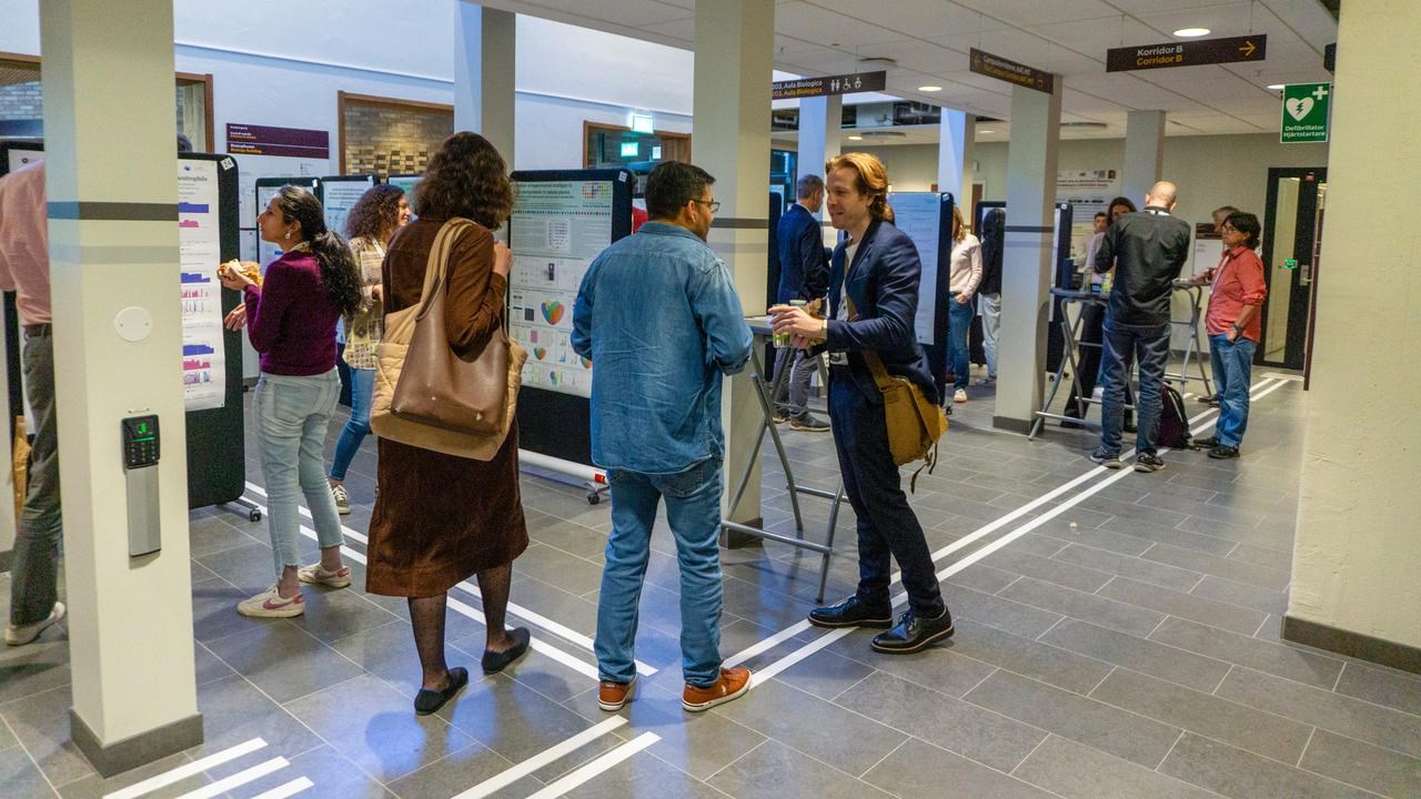 Personer samtalar i sm&aring; grupper framf&ouml;r vetenskapliga postrar i en universitetskorridor.