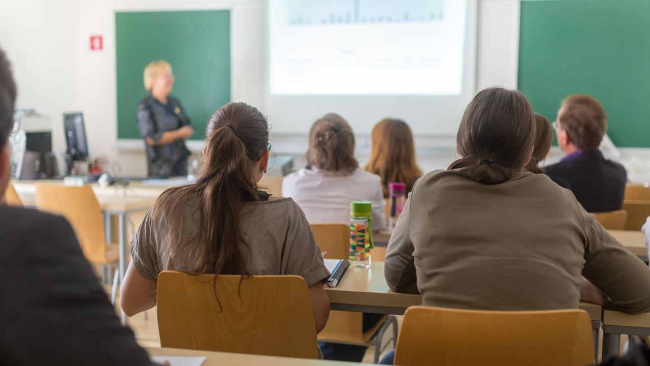 Föreläsningssal på universitet med studenter i förgrunden och en lärare vid tavlan.