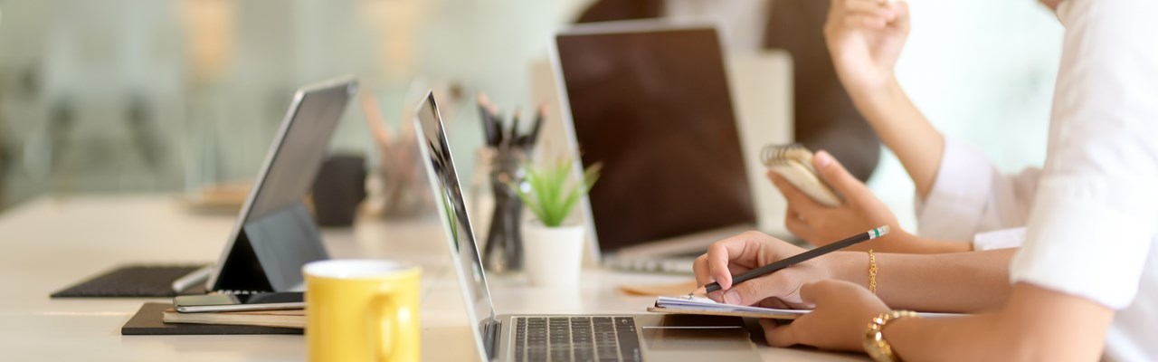 Detaljbild från ett mötesrum med personer och datorer.