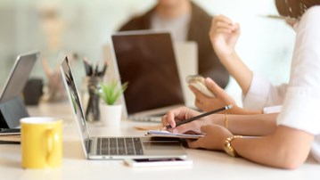 Detaljbild från ett mötesrum med personer och datorer.