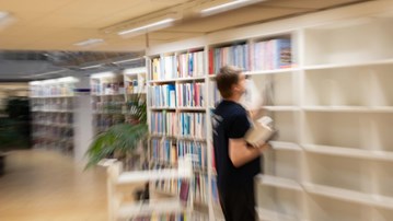 En person ställer in böcker i en bokhylla.