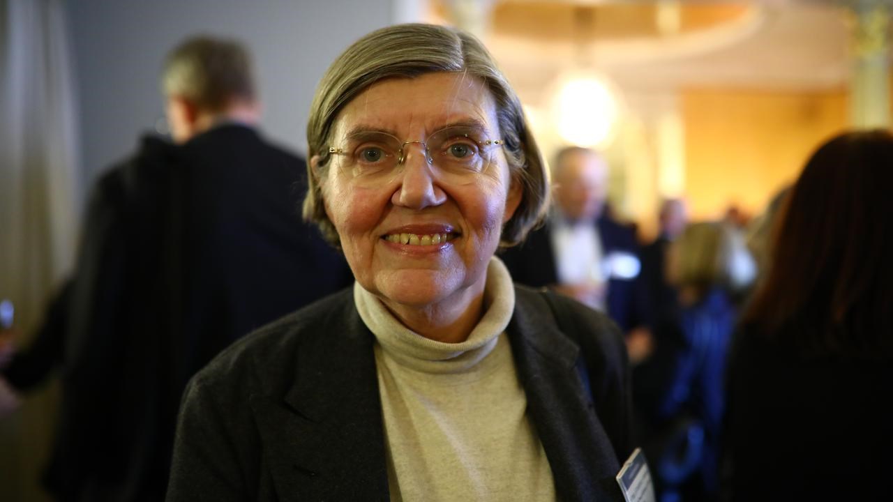 En kvinna med glasögon står framför en grupp människor.