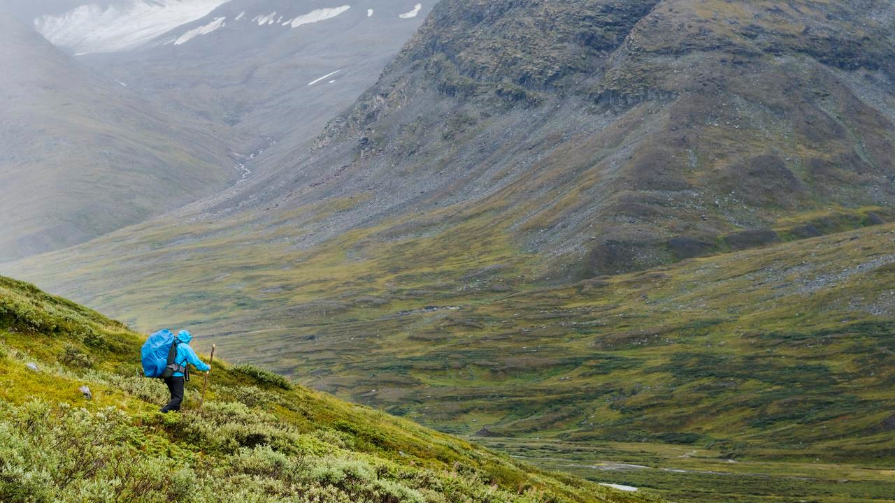 En person med en blå ryggsäck som går nedför ett fjäll.