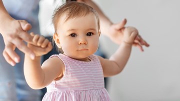 Liten flicka lär sig gå med hjälp av sin mamma.