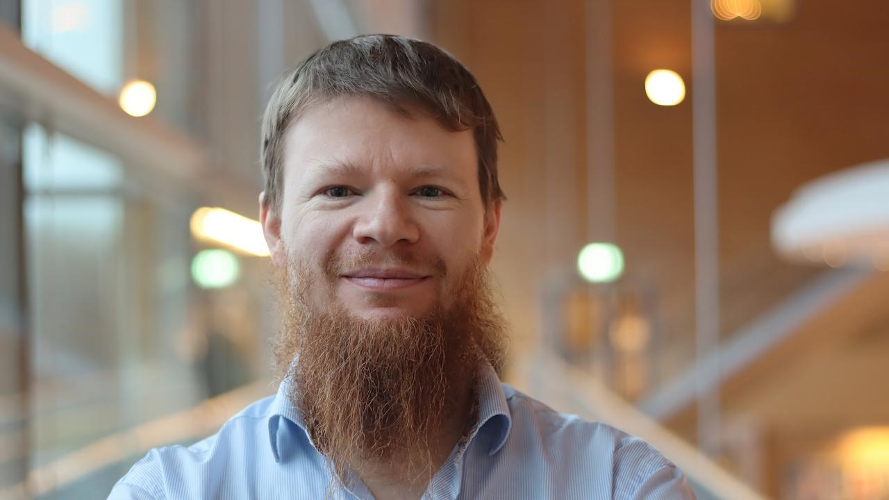 Alexandre Bartel i kort hår och skägg, står vid fönstret i ljusblå skjorta