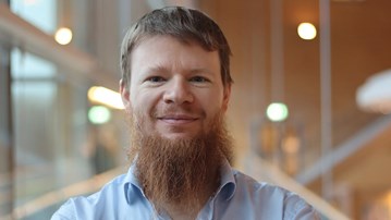 Alexandre Bartel i kort hår och skägg, står vid fönstret i ljusblå skjorta