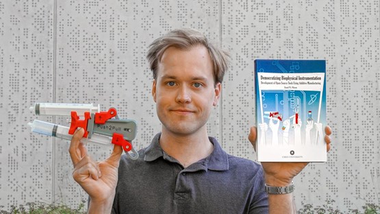 En man som håller upp en bok och ett forskningsinstrument.
