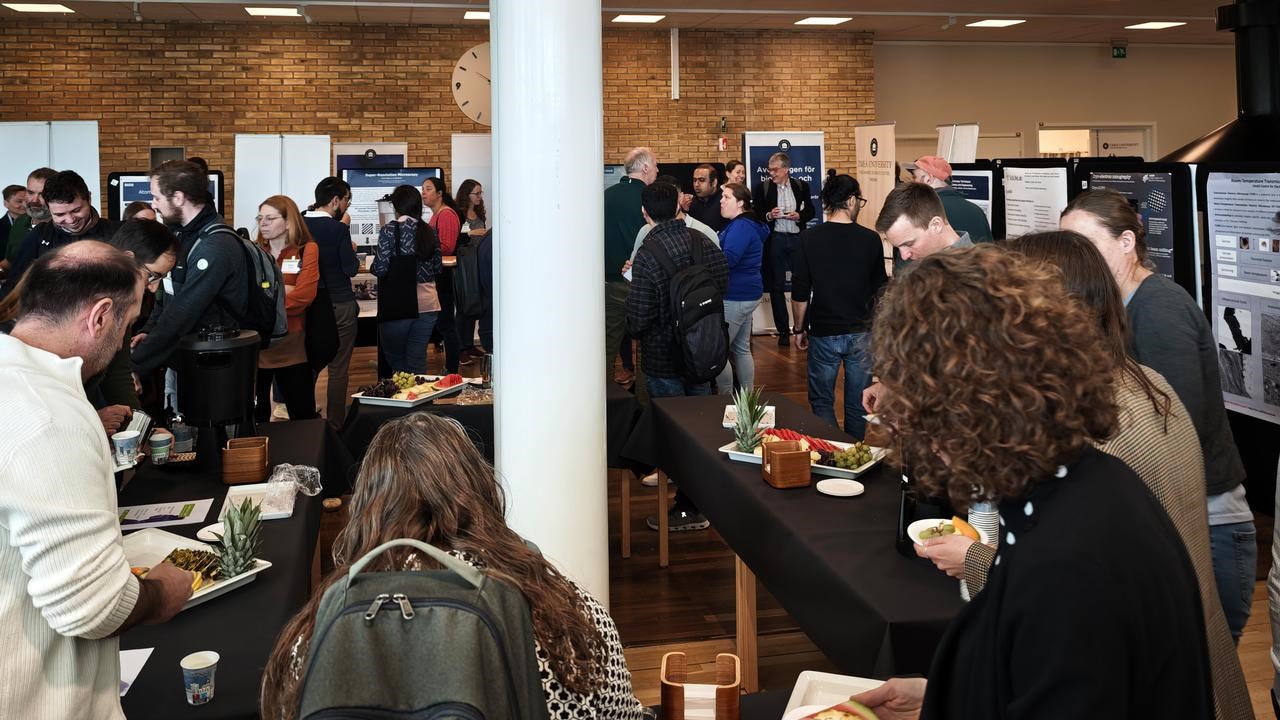A group of people standing around tables during the poster session at the scientific conference