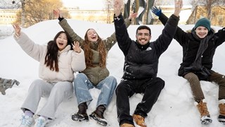 Leende studenter på en snöhög med armarna i luften