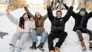 Leende studenter på en snöhög med armarna i luften