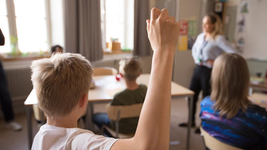 Mellanstadiebarn i klassrum. Pojke räcker upp handen.
