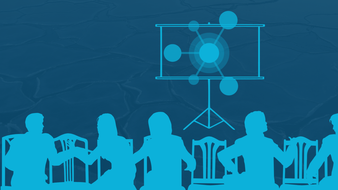 A group of people sitting at a table in front of a projector screen