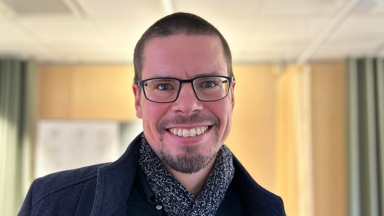 Mörkhårig man med glasögon ler mot kameran.