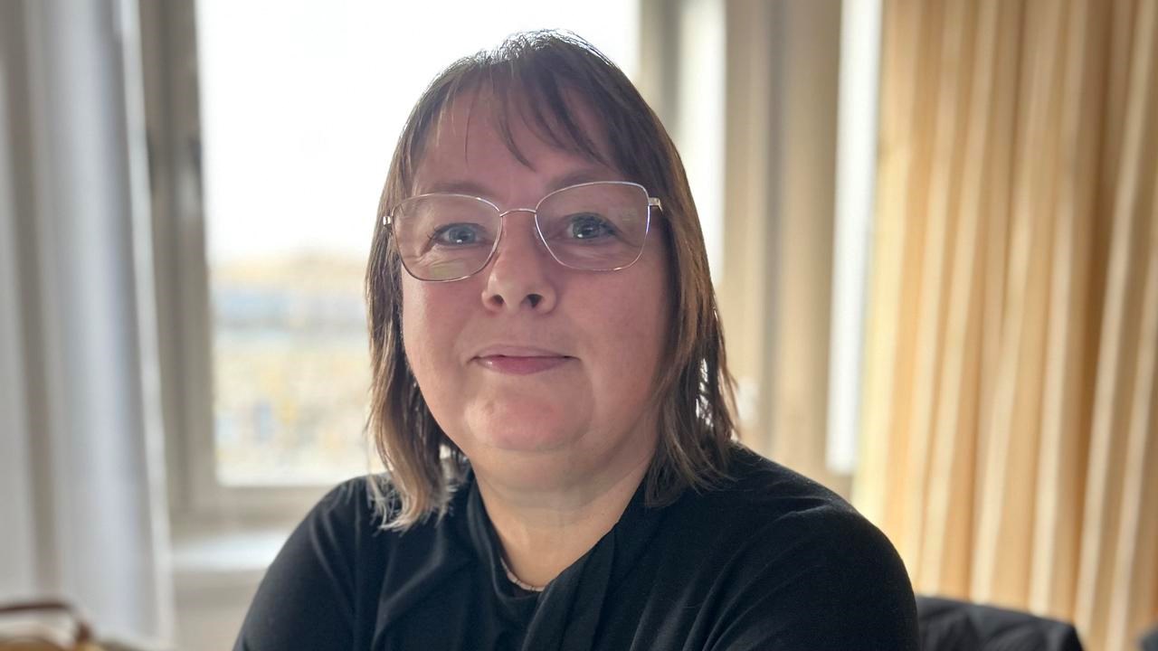 En kvinna som sitter vid ett bord med armarna i kors.