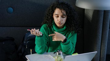 Studenten Sarah pluggar med dator och anteckningsblock.